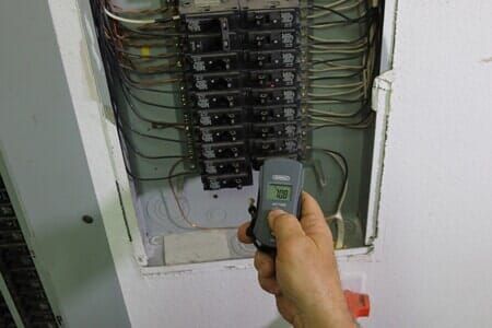 A person is holding a remote control in front of an electrical box.