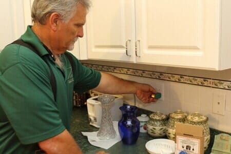 A man in a green shirt is adjusting a light switch in a kitchen.