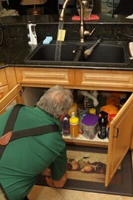 A man is looking under the sink in a kitchen.