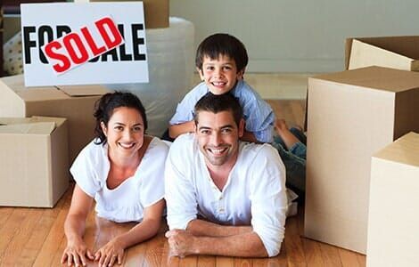 A family is laying on the floor in front of a for sale sign