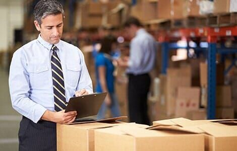A man is standing in a warehouse looking at a clipboard.