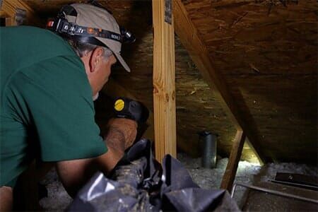 A man wearing a headlamp is working in an attic.