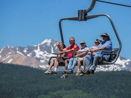 A group of people are riding a ski lift with mountains in the background.
