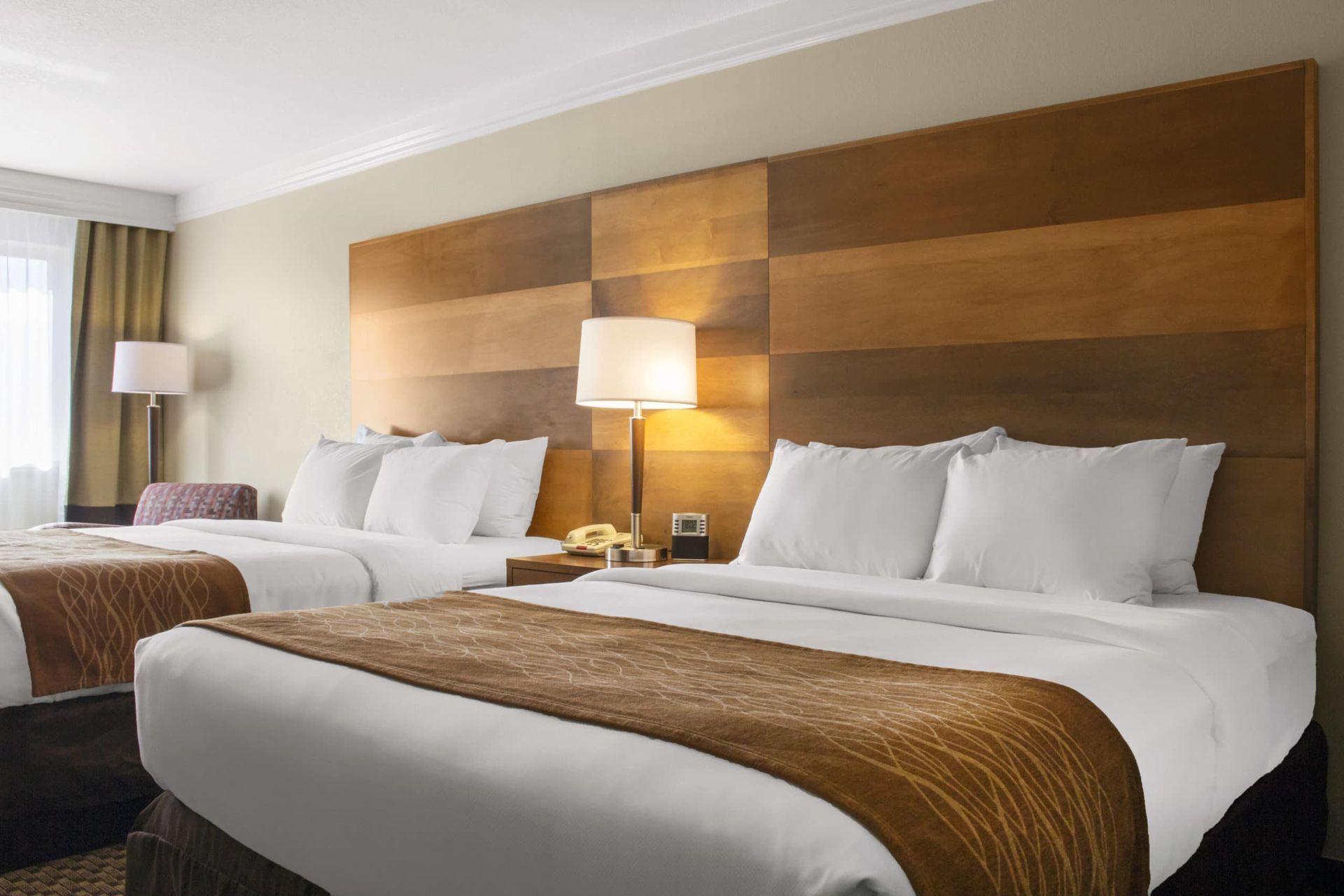 A hotel room with two beds and a wooden headboard.