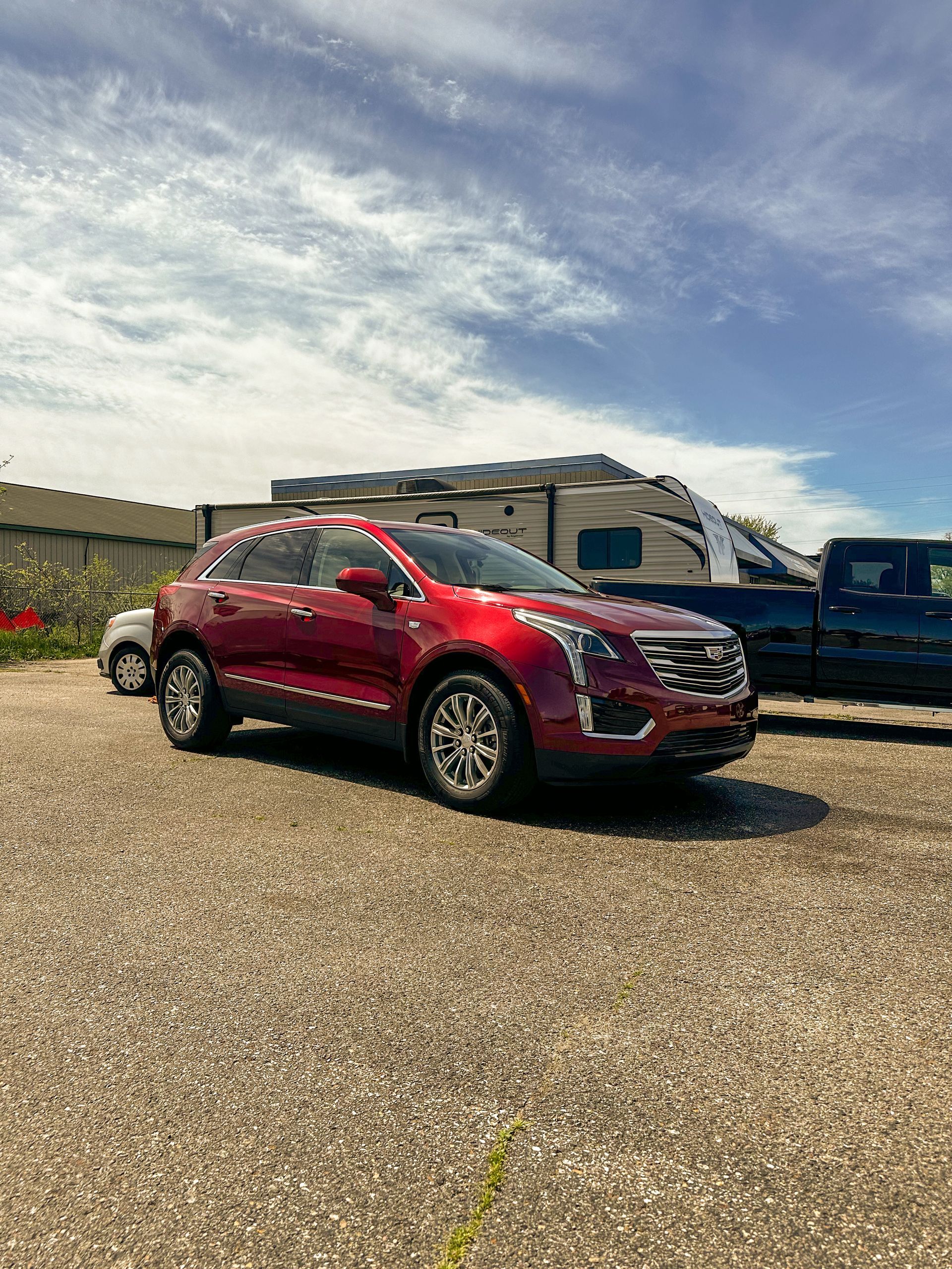 A red car is parked in a gravel lot next to a trailer.