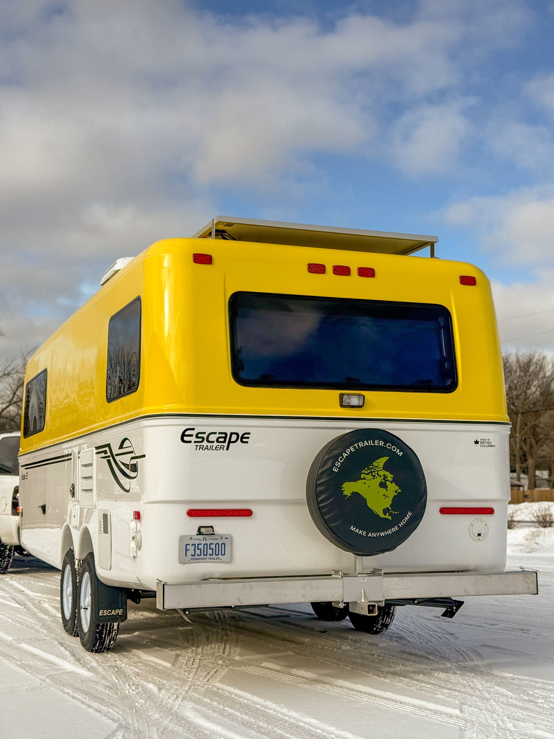 Yellow Escape trailer on snowy ground, viewed from the rear against a cloudy sky.