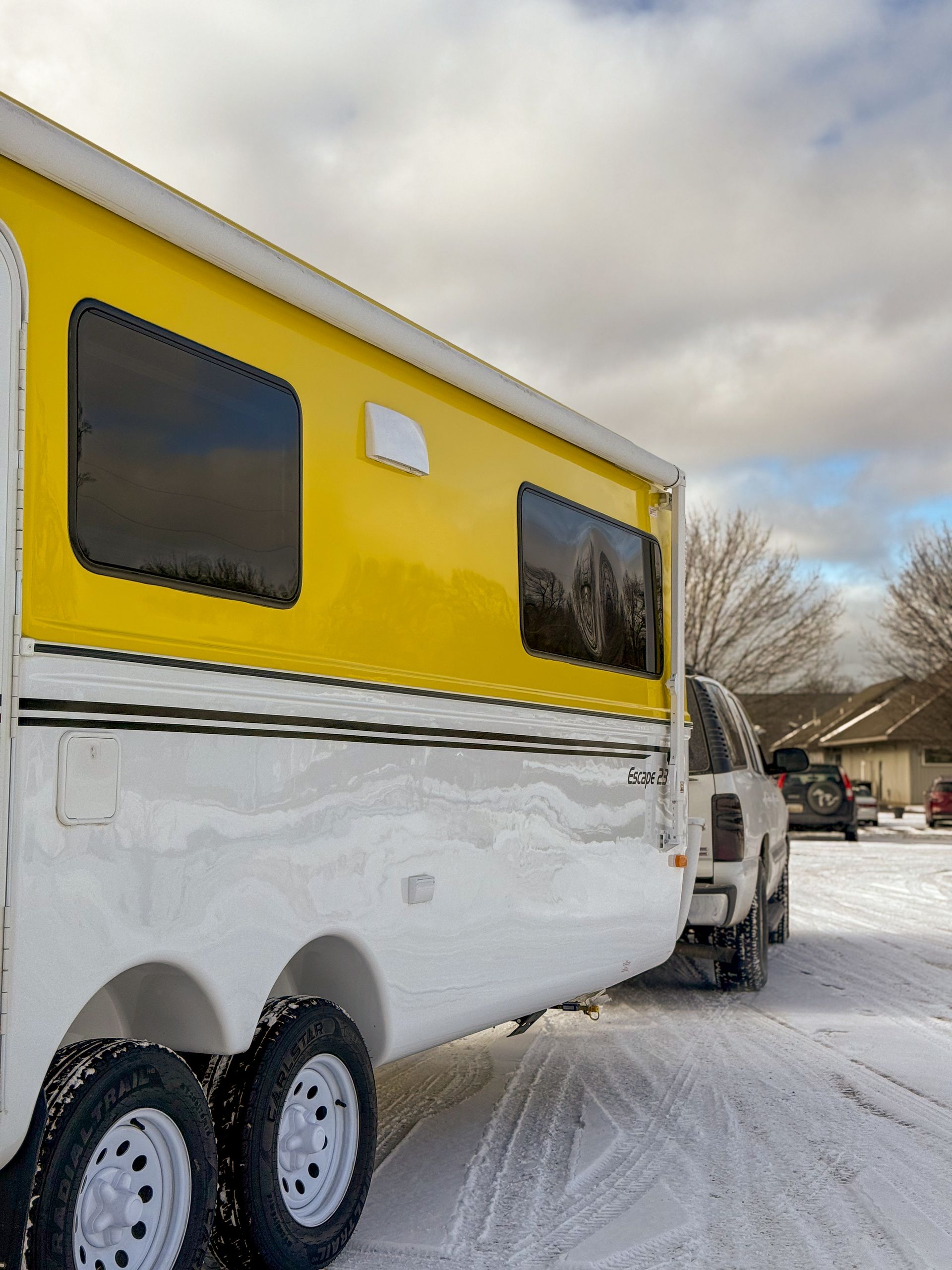 Yellow and white camper trailer parked in snow under a cloudy sky