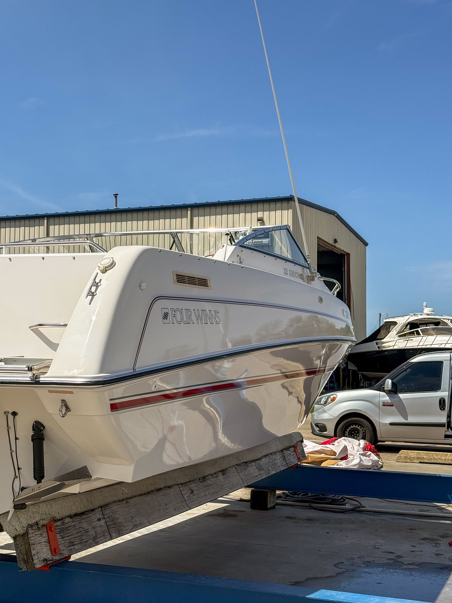 Damaged white boat on a trailer at a boatyard, with debris and a white SUV nearby