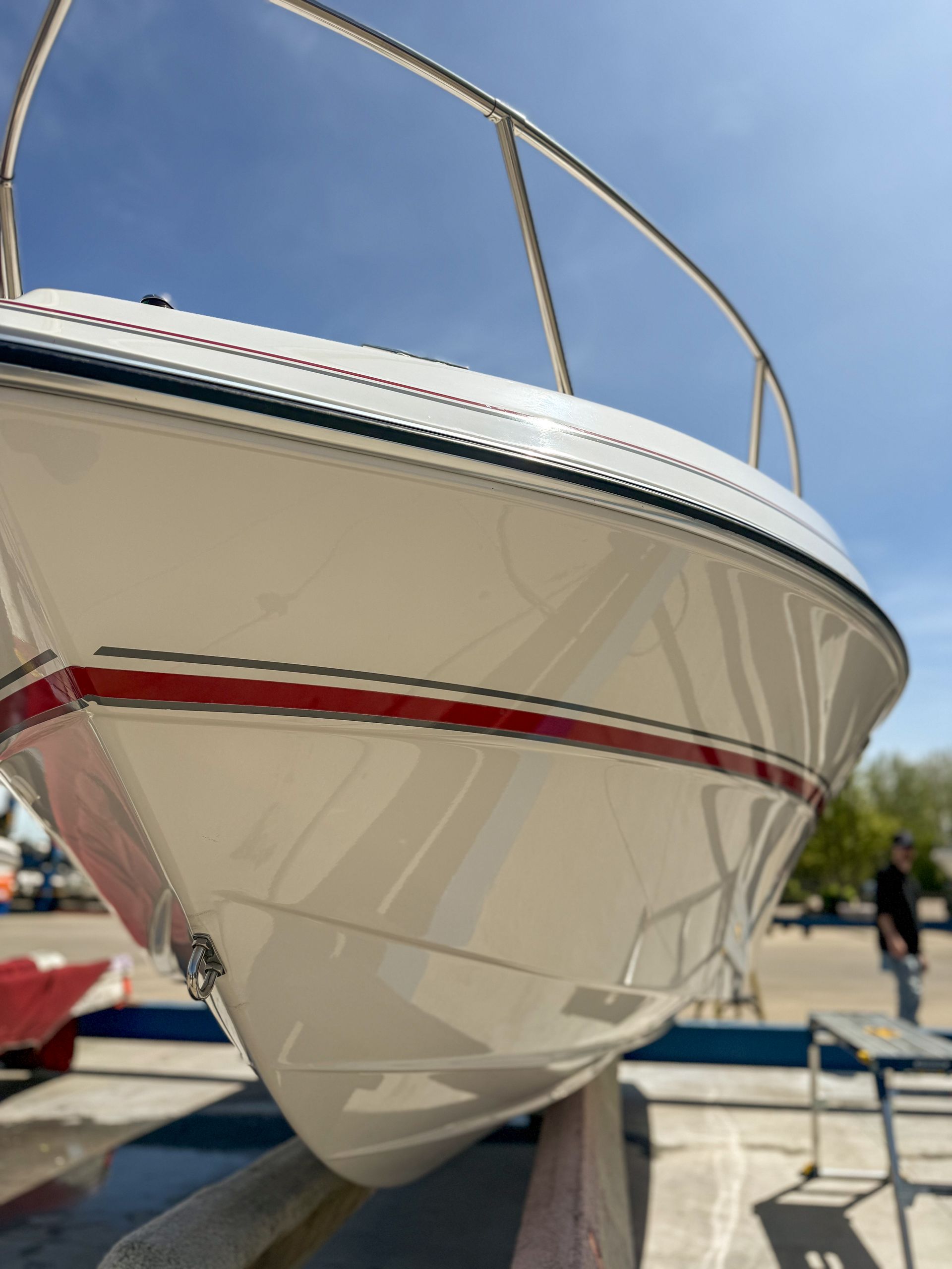 White sailboat hull with red stripe on a boat trailer at a marina, viewed from the bow