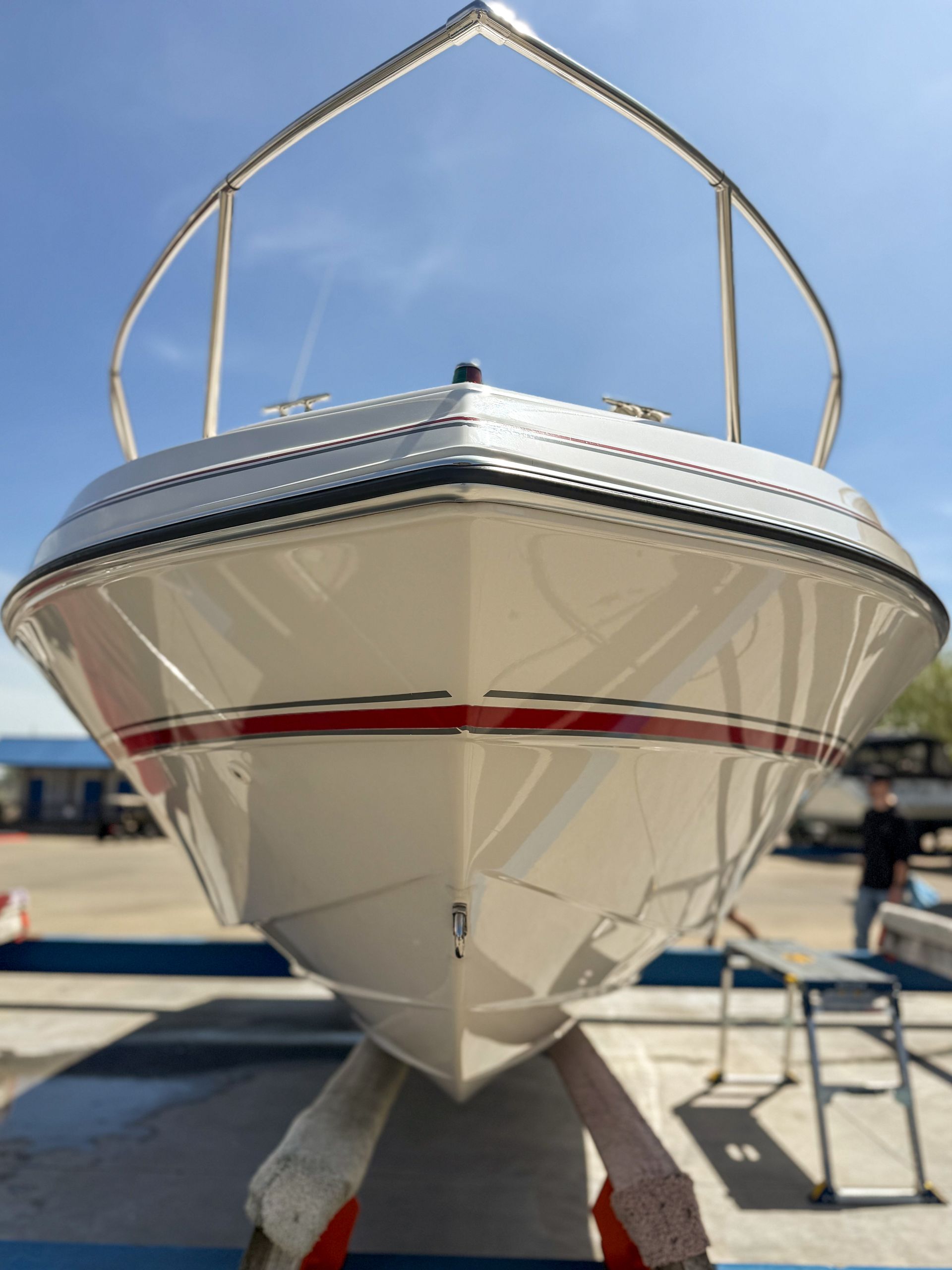 Front view of a white motorboat on a trailer at a boatyard, with a red stripe and support arch overhead