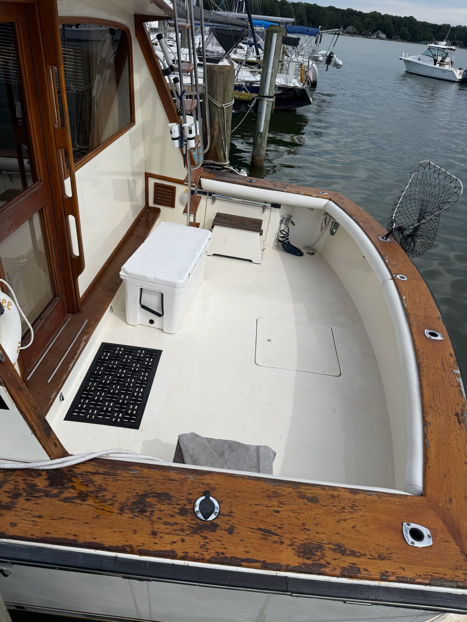 Empty white boat deck with wooden trim and marina water in the background