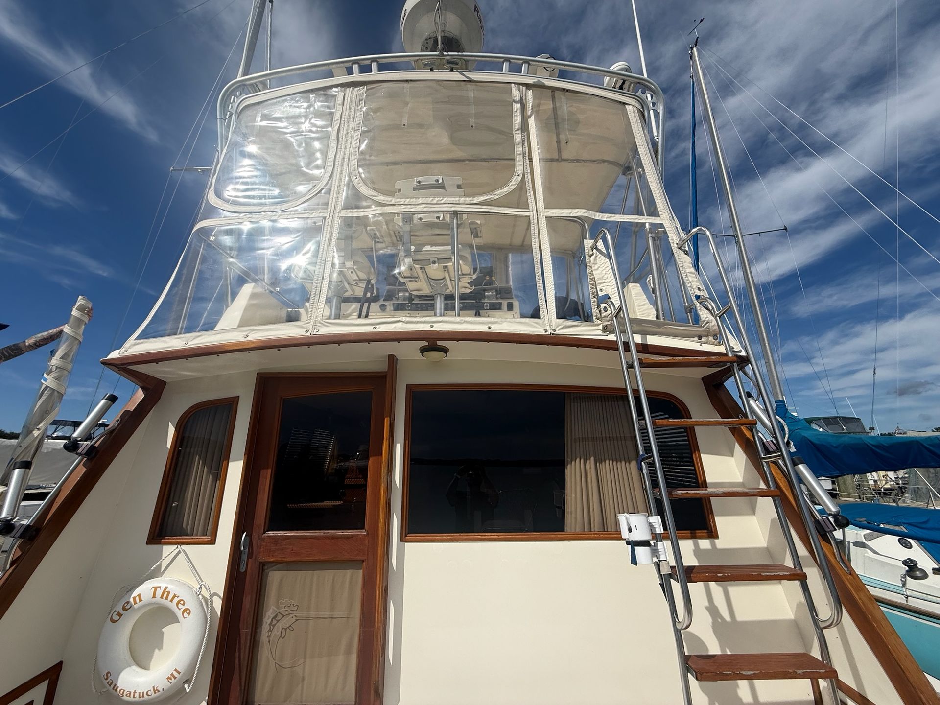 Boat deck cabin beneath a white radar arch against a bright blue sky with rigging and ladders