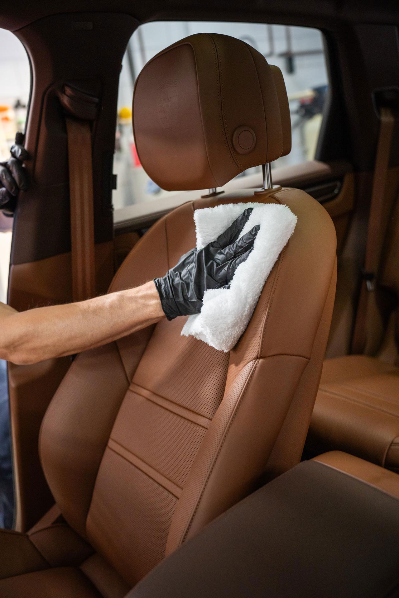 A person is cleaning a brown leather car seat with a towel.
