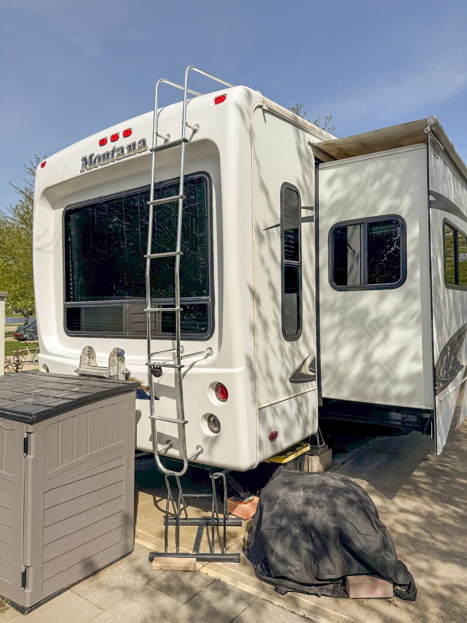 White RV with rear ladder parked outdoors beside a utility box on a sunny day