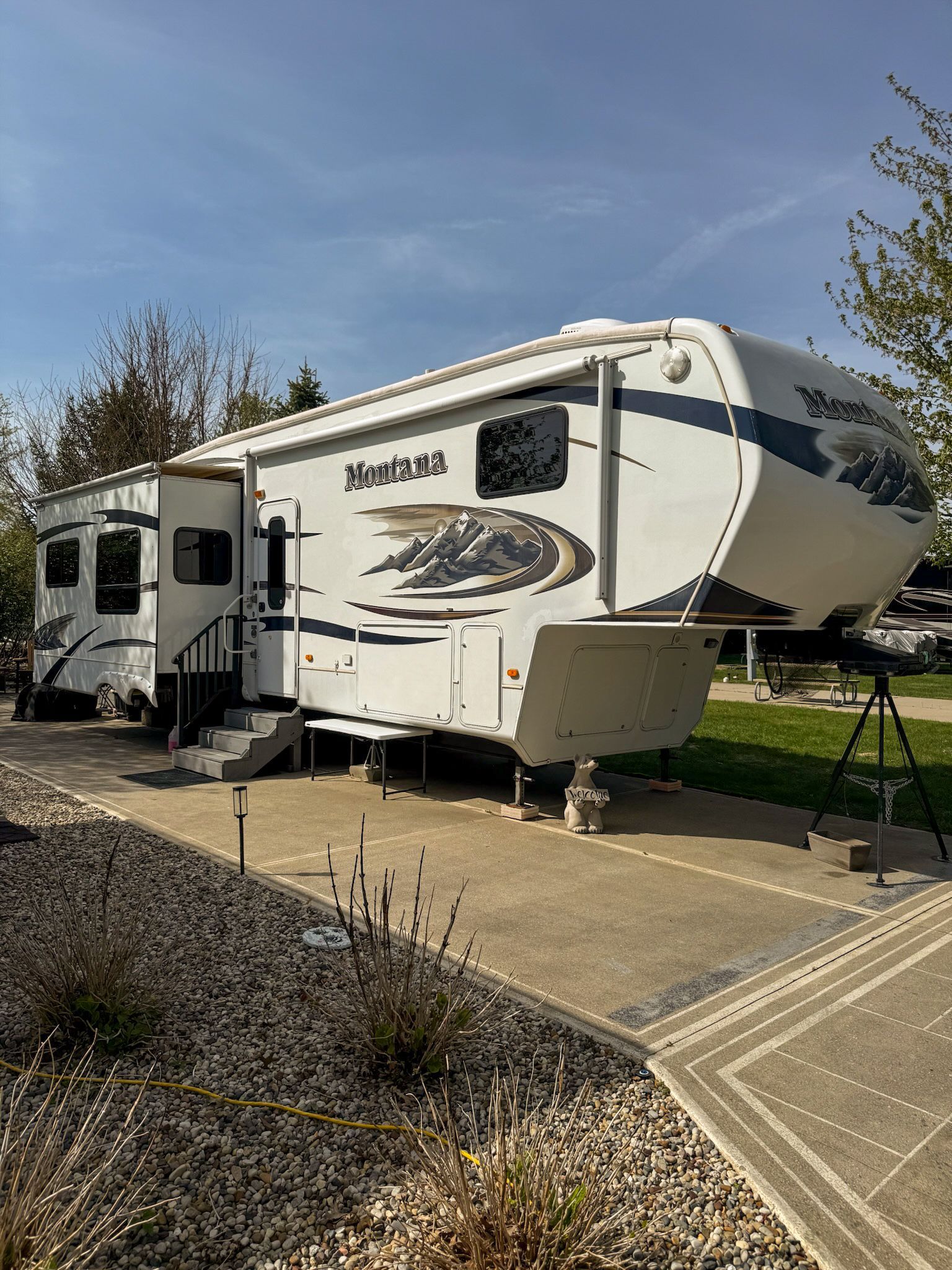 White Jayco North Point fifth-wheel RV parked on a concrete pad beside a landscaped gravel driveway.