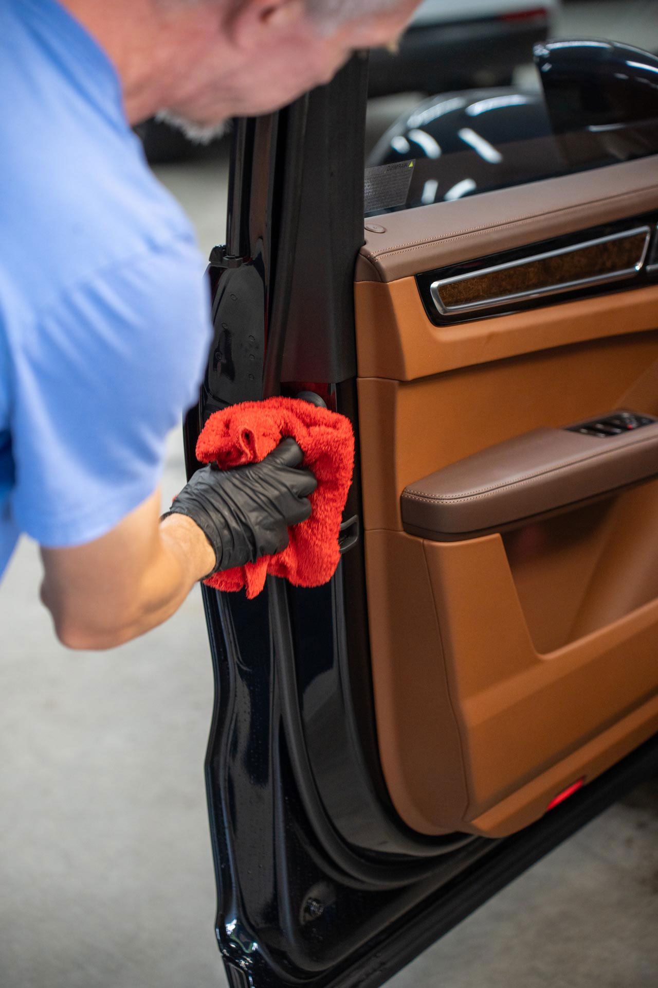 A man is cleaning the door of a car with a microfiber.