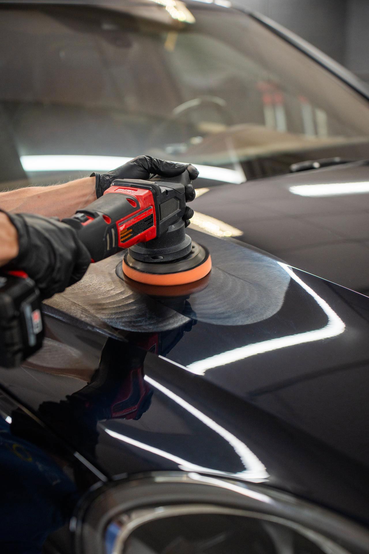 A person is polishing the hood of a car with a machine.