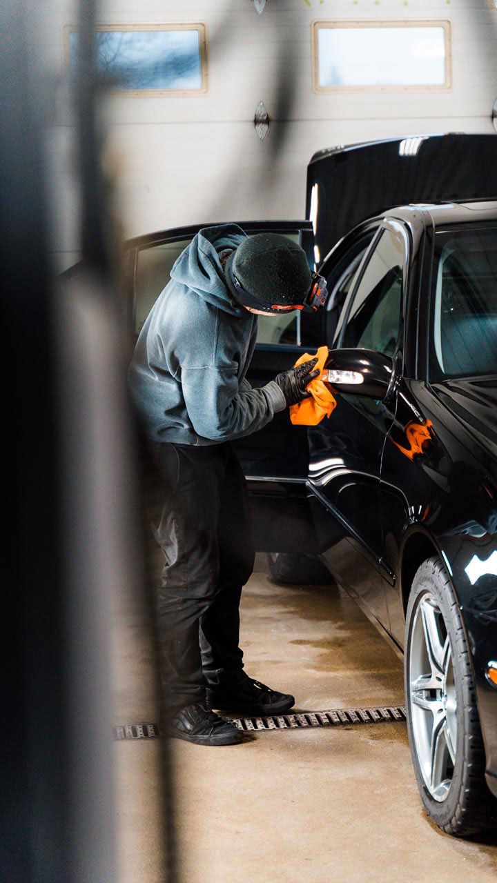 A man is polishing a black car in a garage.