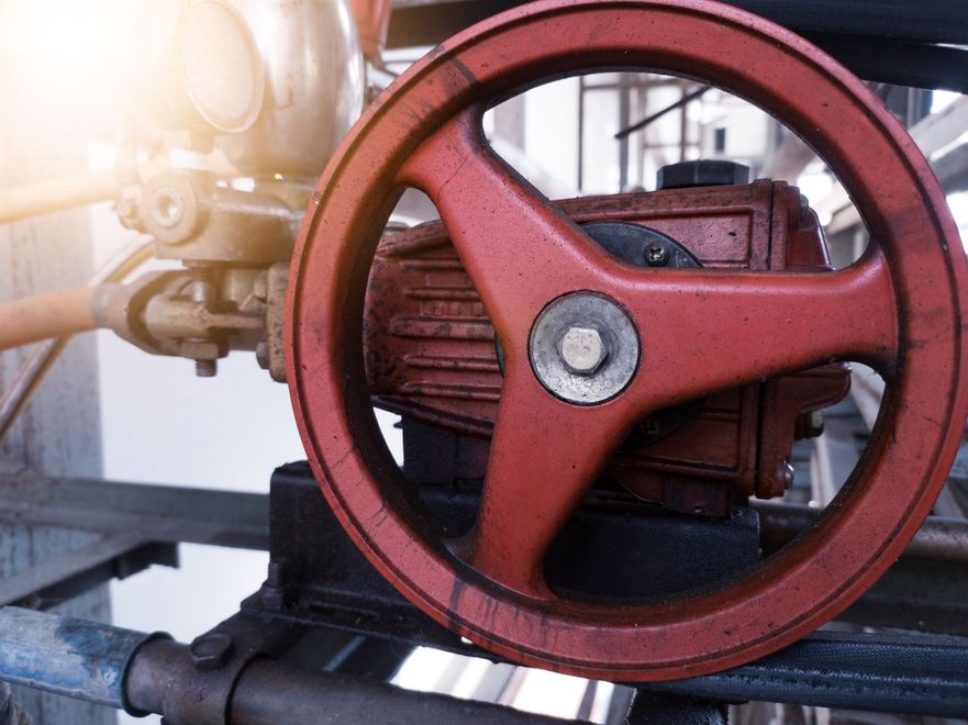 Red industrial valve wheel on piping with sunlight flare in an industrial setting