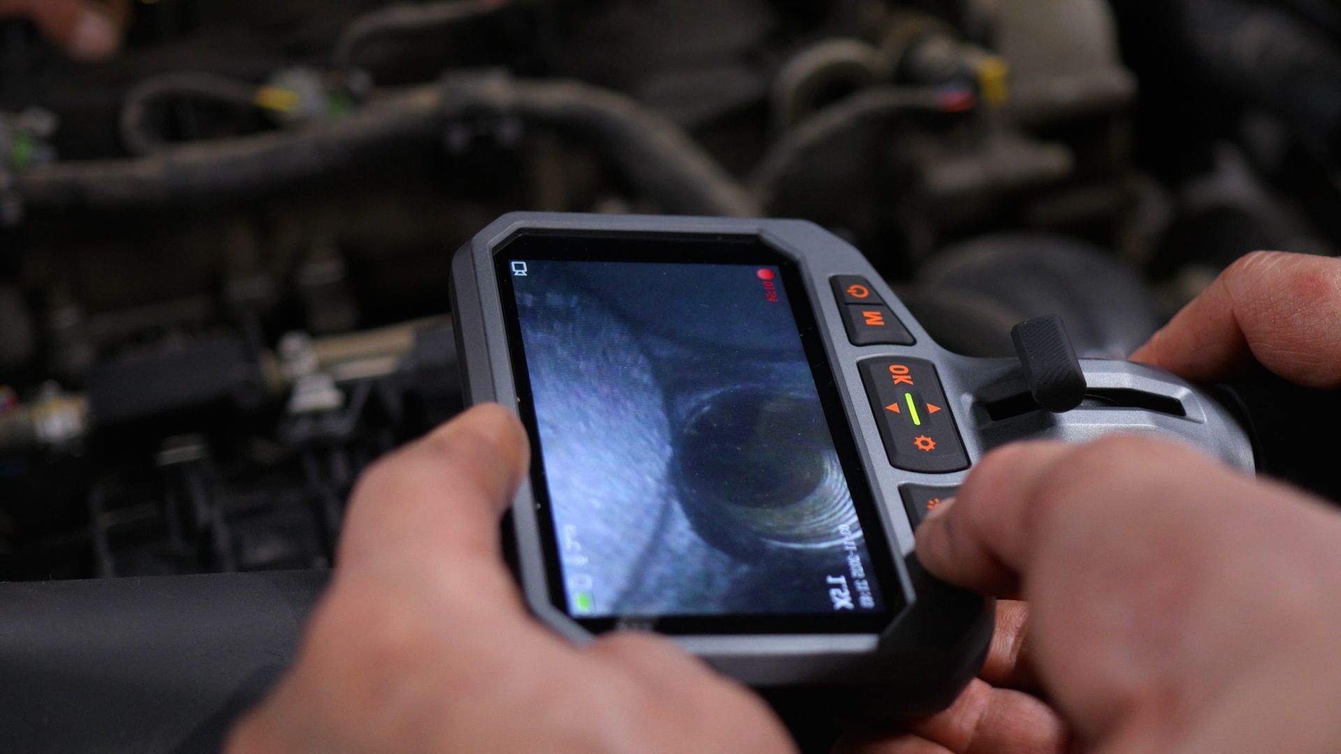 Hands holding a handheld inspection camera showing a close-up inside an engine compartment. Hands holding a handheld inspection camera showing a close-up inside an engine compartment.