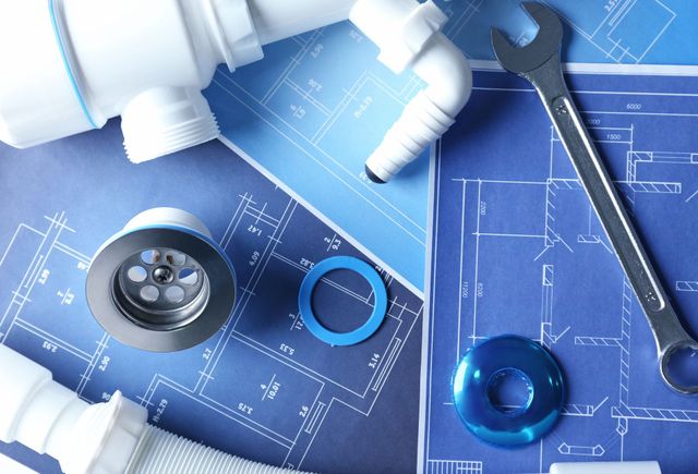 Plumbing tools and fittings on blue technical blueprints, including a wrench, pipes, and tape measure