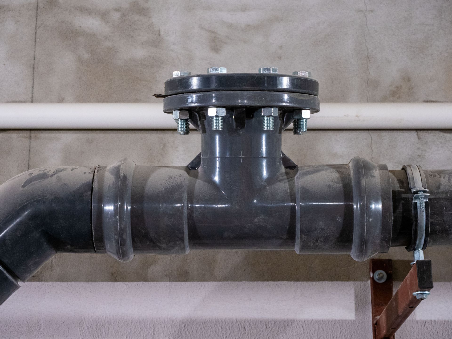 Black industrial pipe with a flanged vertical branch against a gray wall Black industrial pipe with a flanged vertical branch against a gray wall