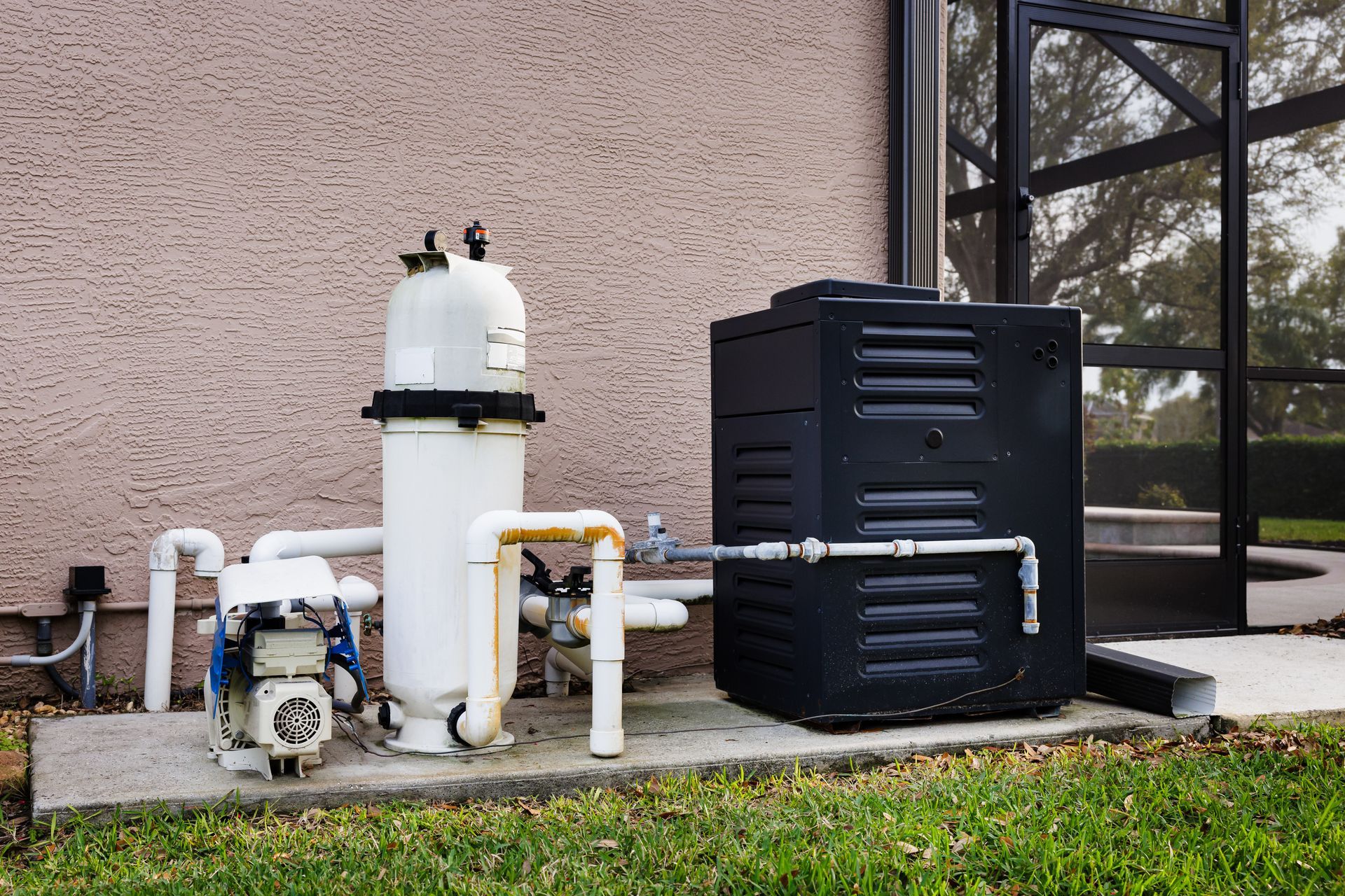 Outdoor pool equipment: white pipes, pump, filter, and black heater units beside a house wall Outdoor pool equipment: white pipes, pump, filter, and black heater units beside a house wall