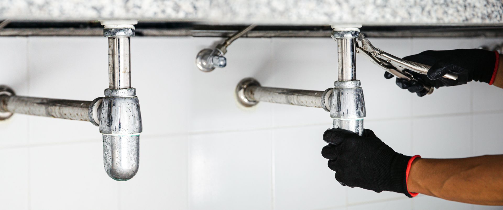 Gloved plumber tightening a chrome sink drain pipe under a bathroom sink. Gloved plumber tightening a chrome sink drain pipe under a bathroom sink.