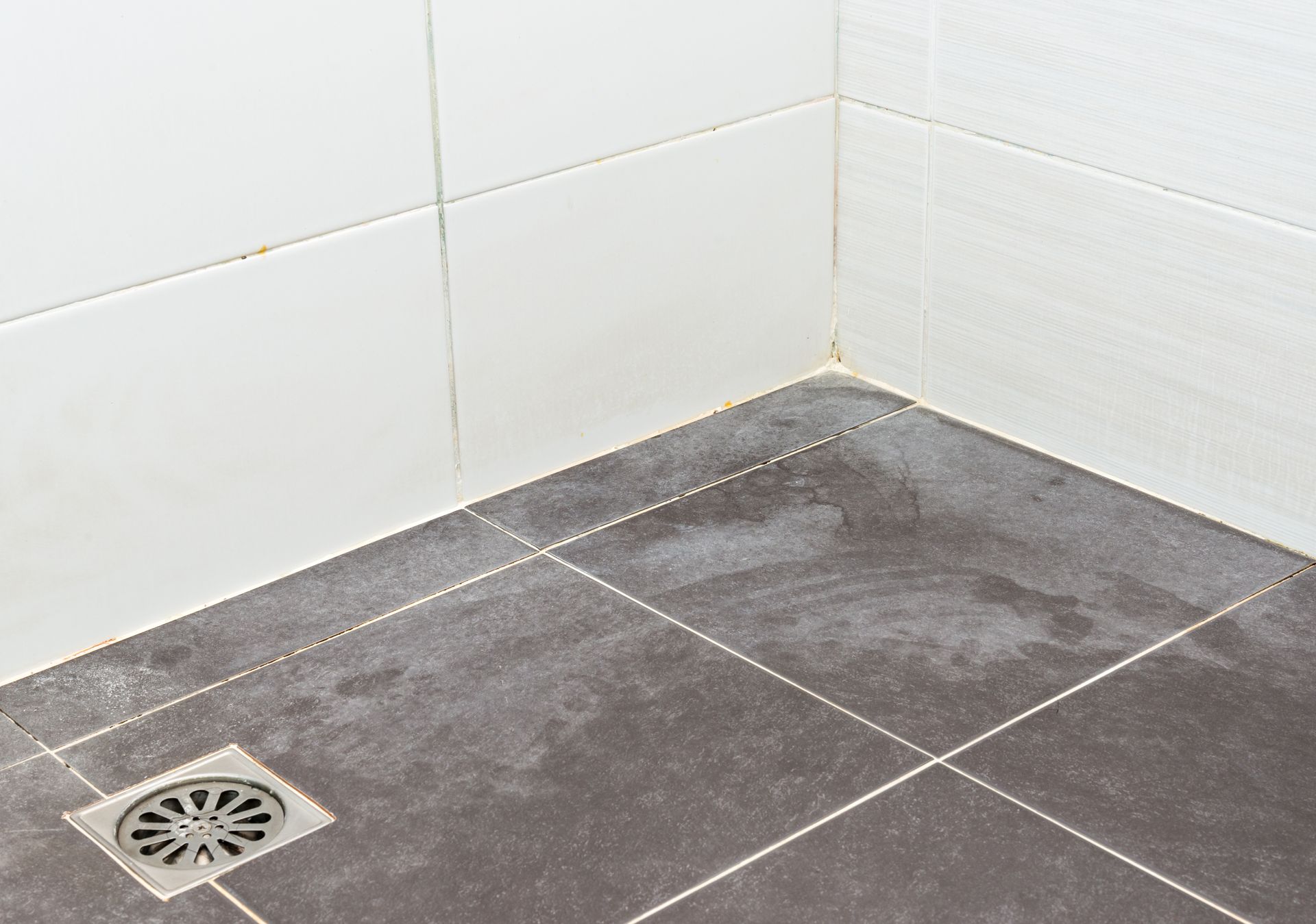 Corner of a tiled shower with a floor drain and dark gray floor tiles. Corner of a tiled shower with a floor drain and dark gray floor tiles.