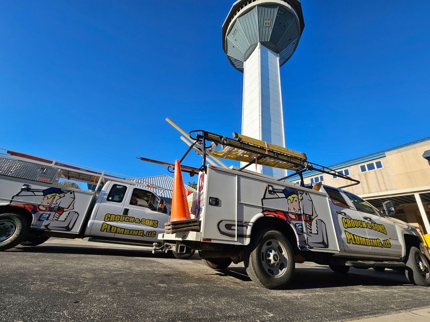 Two utility trucks parked by a tall tower under a clear blue sky