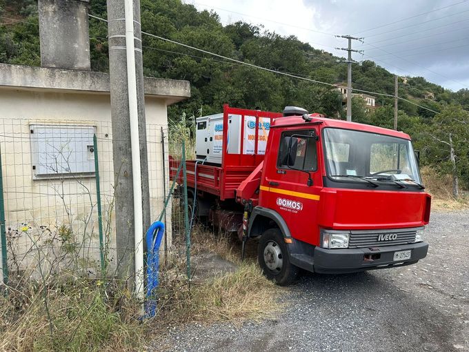 Un camioncino rosso di servizio è parcheggiato accanto a un edificio in cemento deteriorato, sul ciglio di una strada rurale.