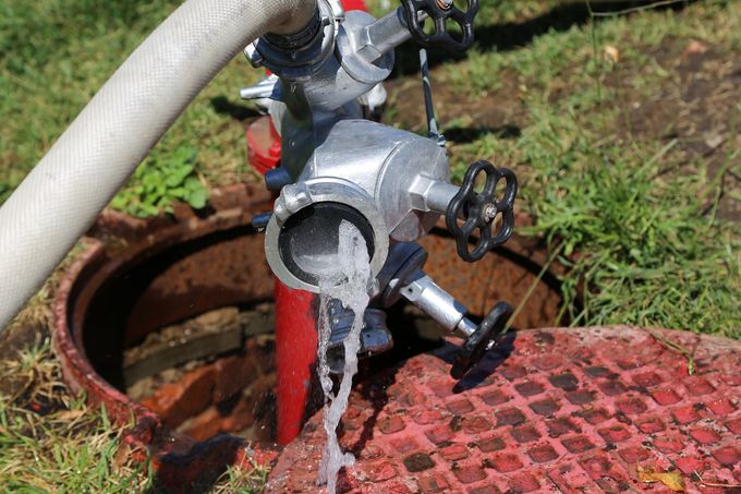 Idrante rosso con getto d'acqua accanto a un tombino sull'erba e una grata rossa