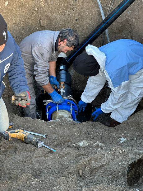 Operai che installano un tubo sotterraneo blu in una trincea in un cantiere edile.