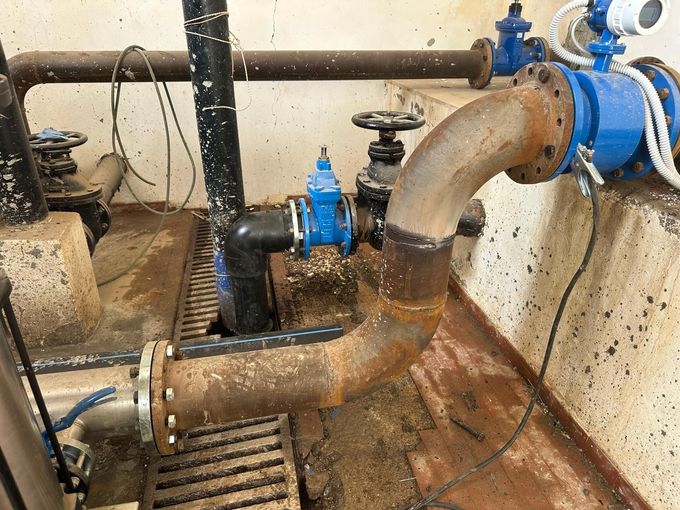 Tubature industriali blu e arrugginite con valvole in un locale tecnico con pareti e pavimento in cemento.