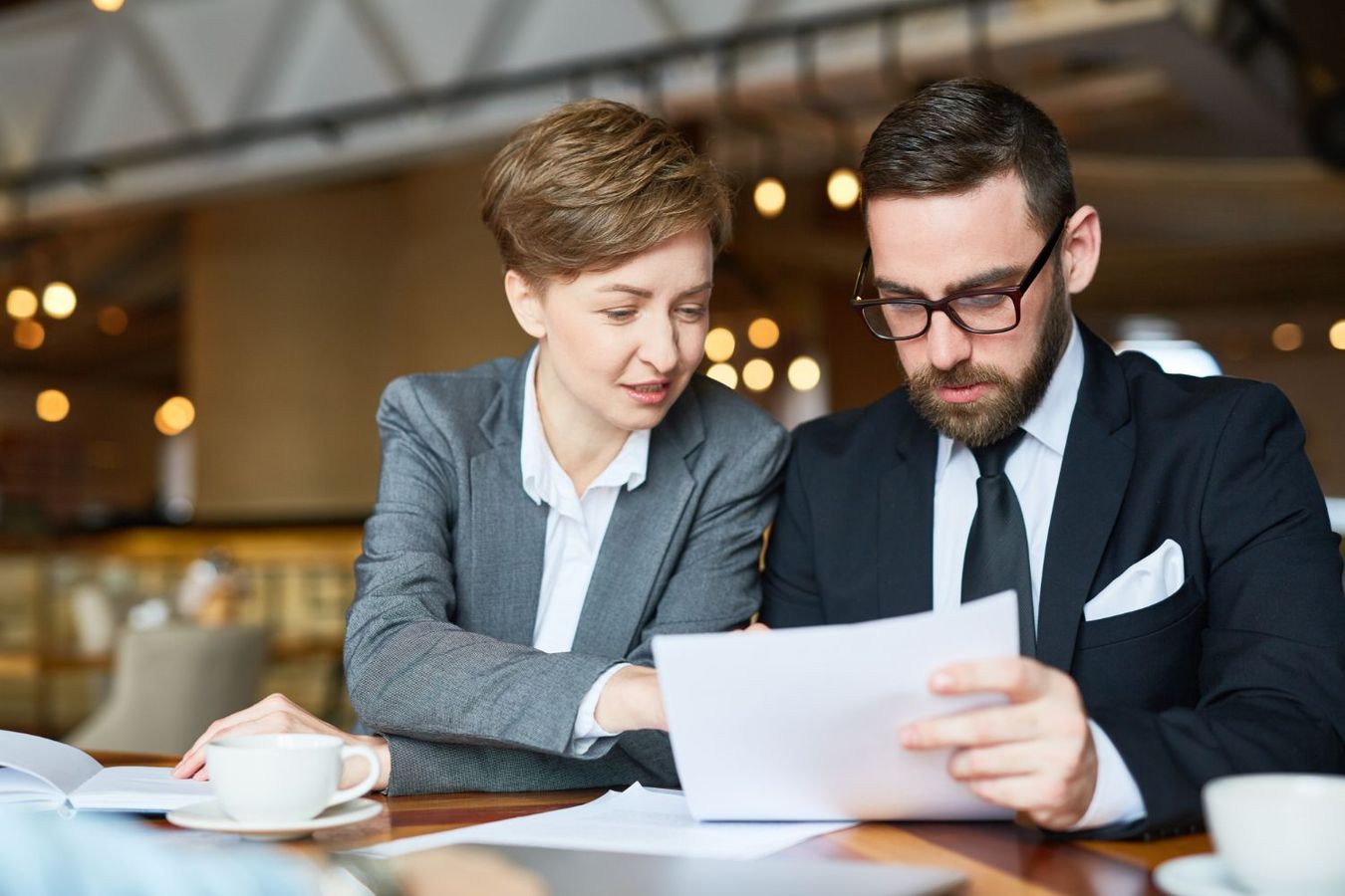Two professionals in business attire reviewing a document together at a table in a café