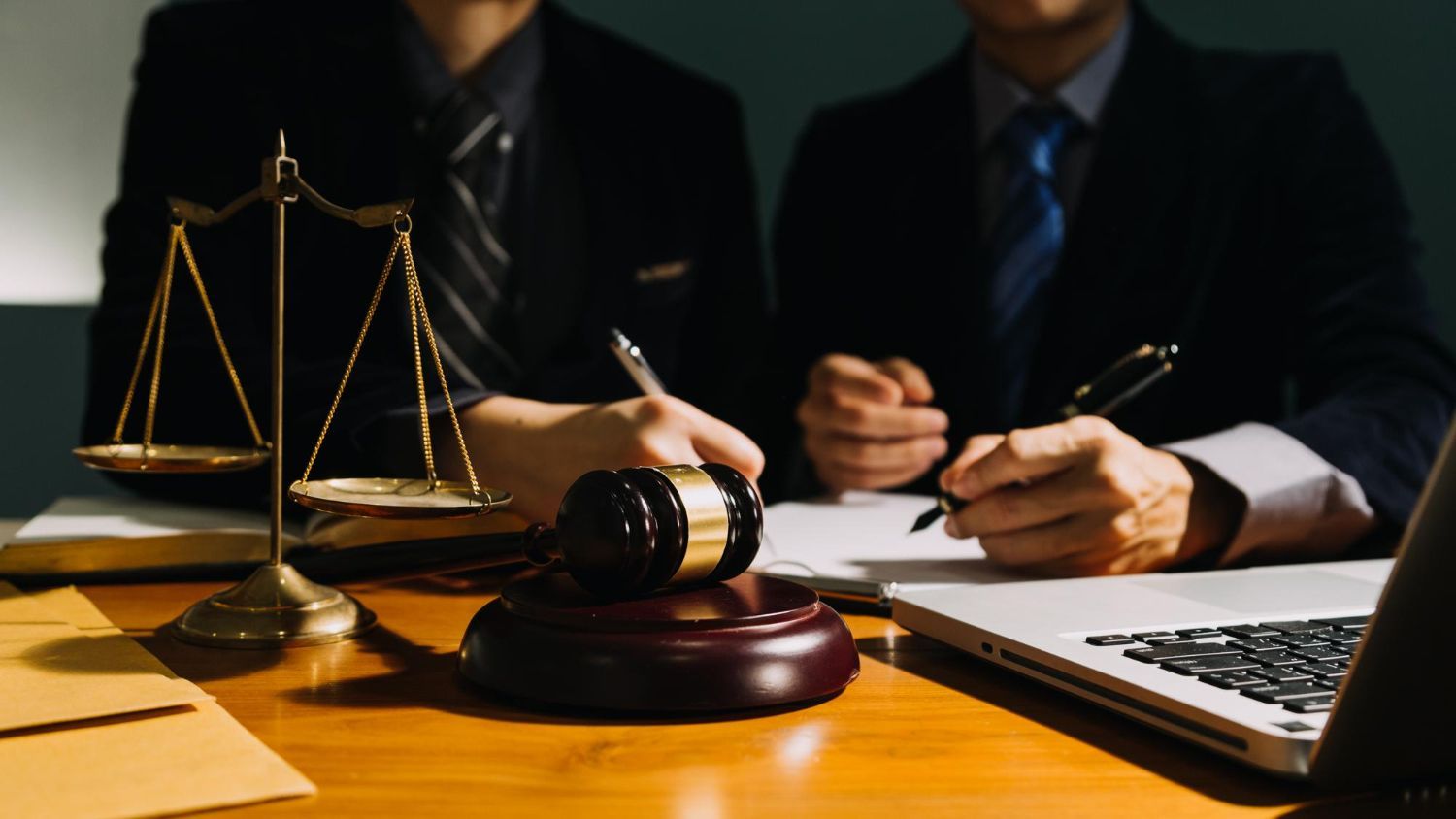Legal consultation scene with scales, gavel, and two suited professionals reviewing documents at a desk