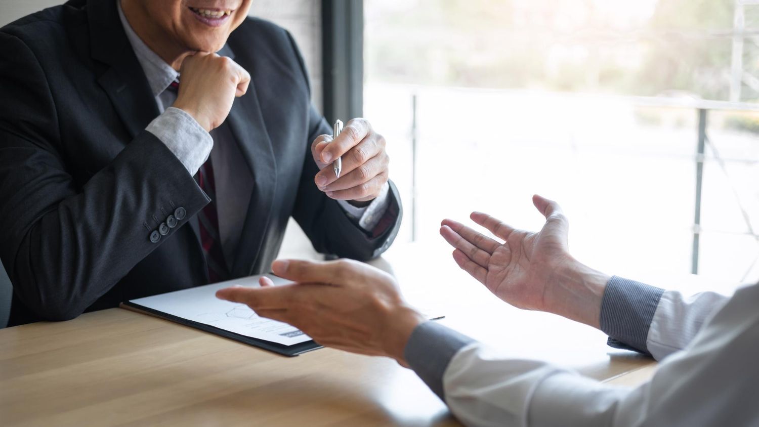 Business meeting with two people gesturing across a wooden table in a bright office