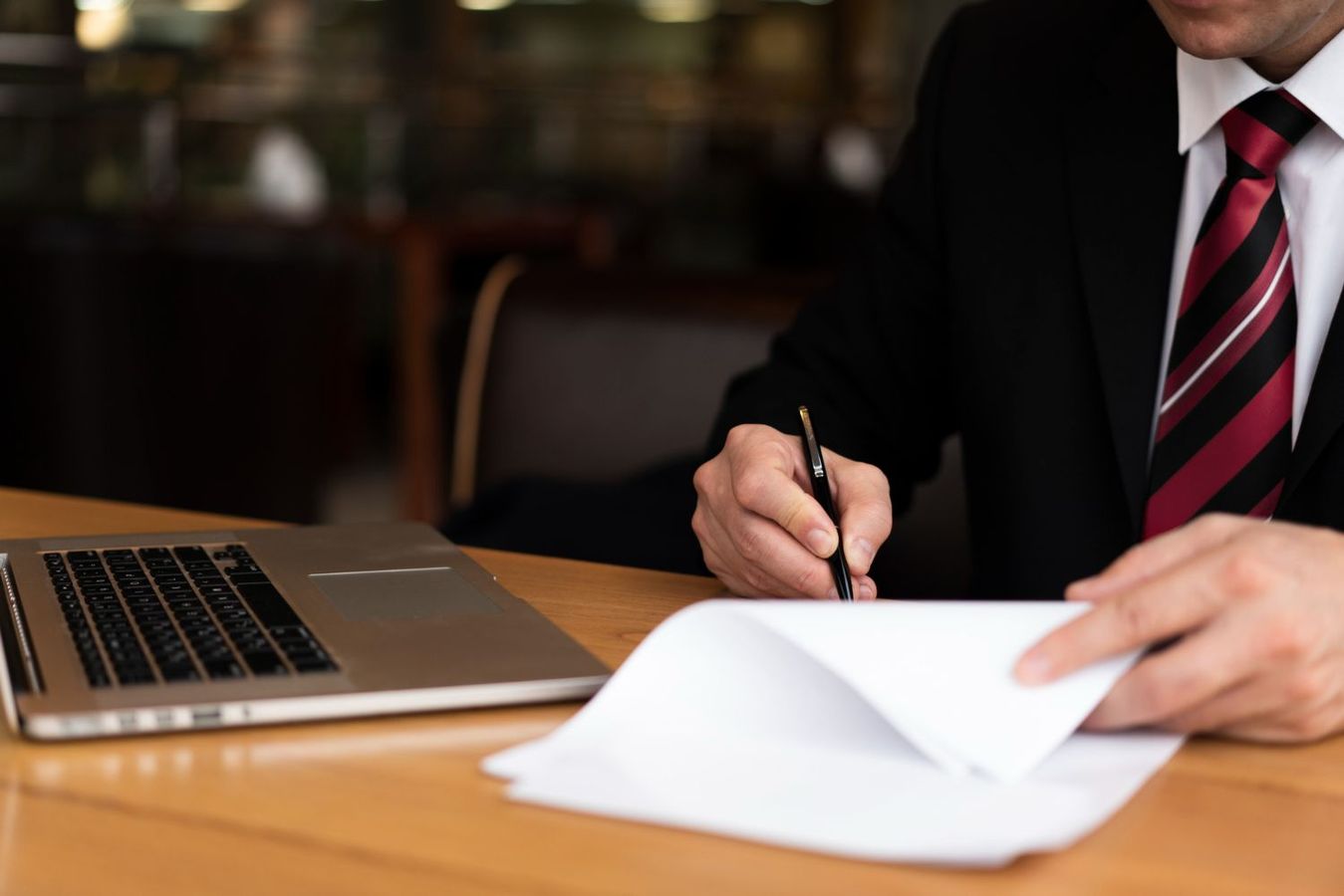 Businessperson signing papers beside a laptop at a wooden desk