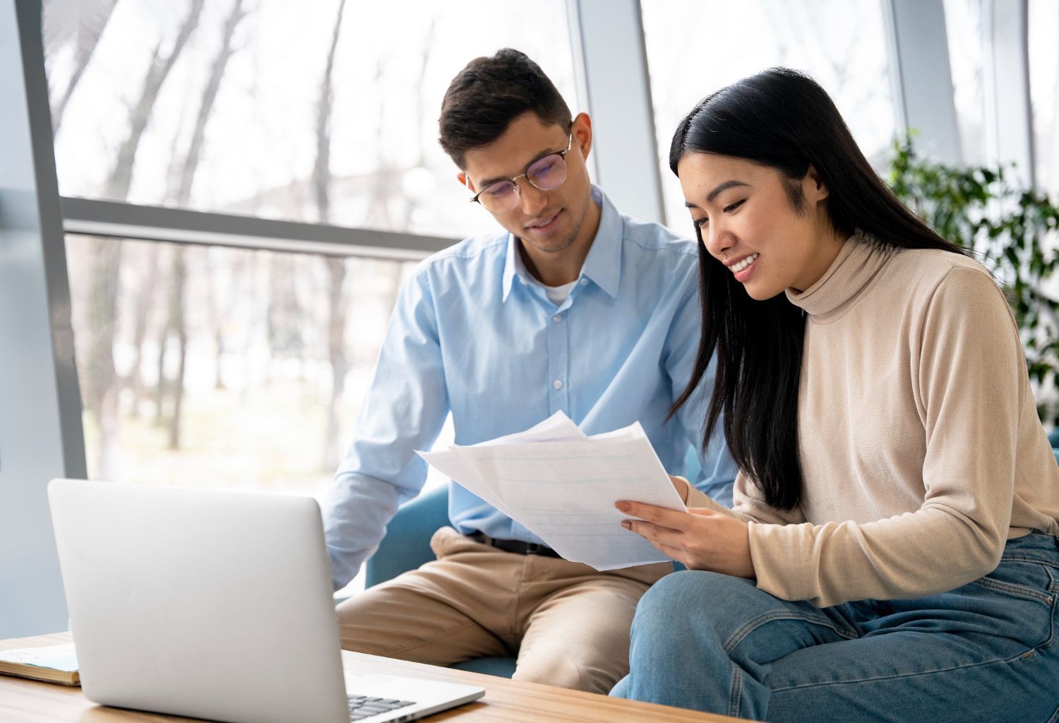 Two people reviewing papers beside a laptop in a bright office setting