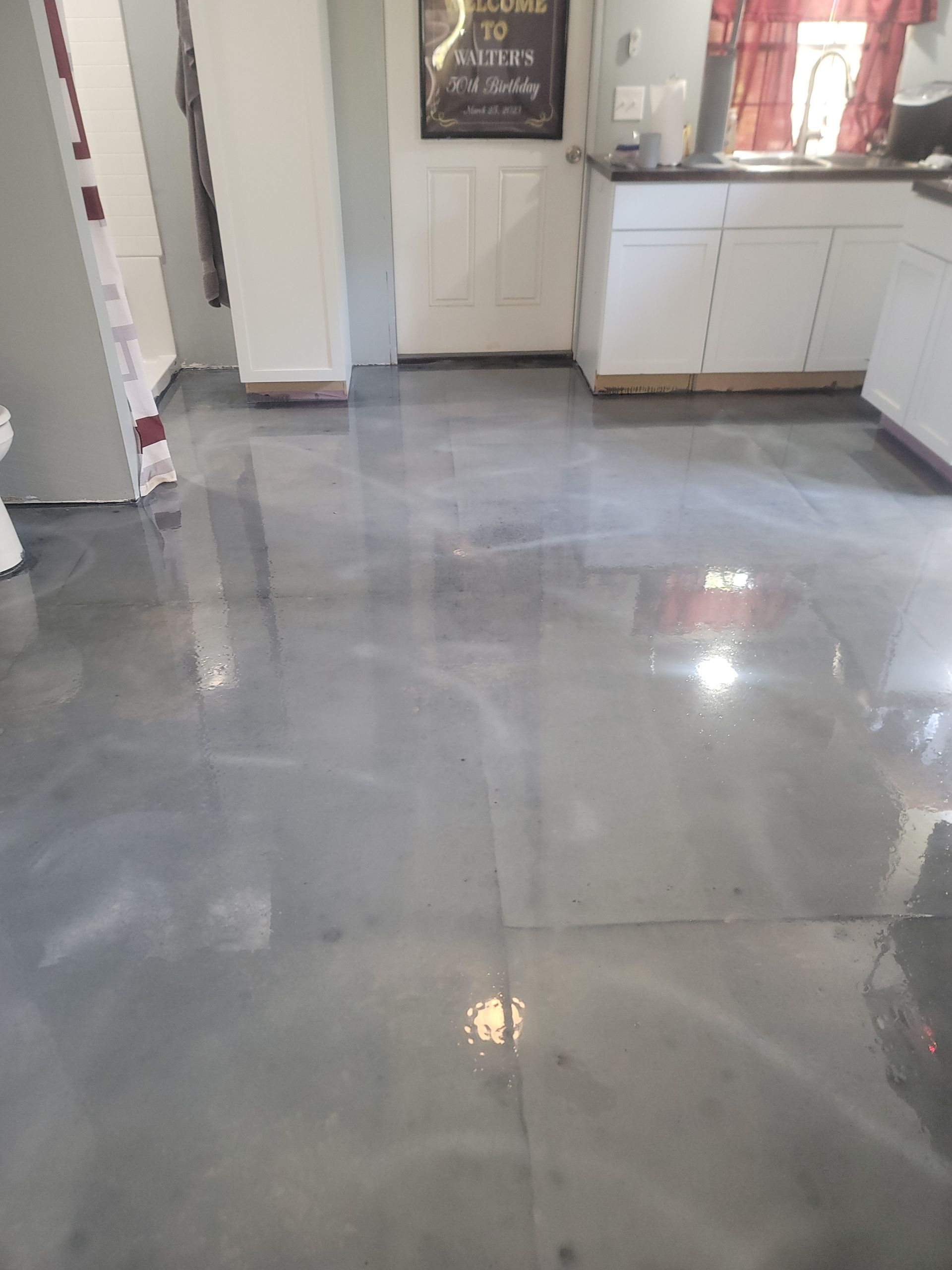 Shiny gray tile floor in a bright indoor room with white cabinets and a window.