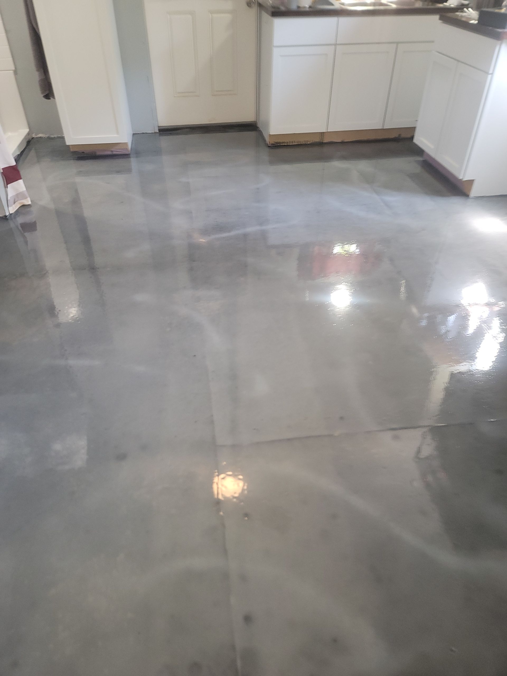Shiny gray tiled kitchen floor with white cabinets and bright light reflections