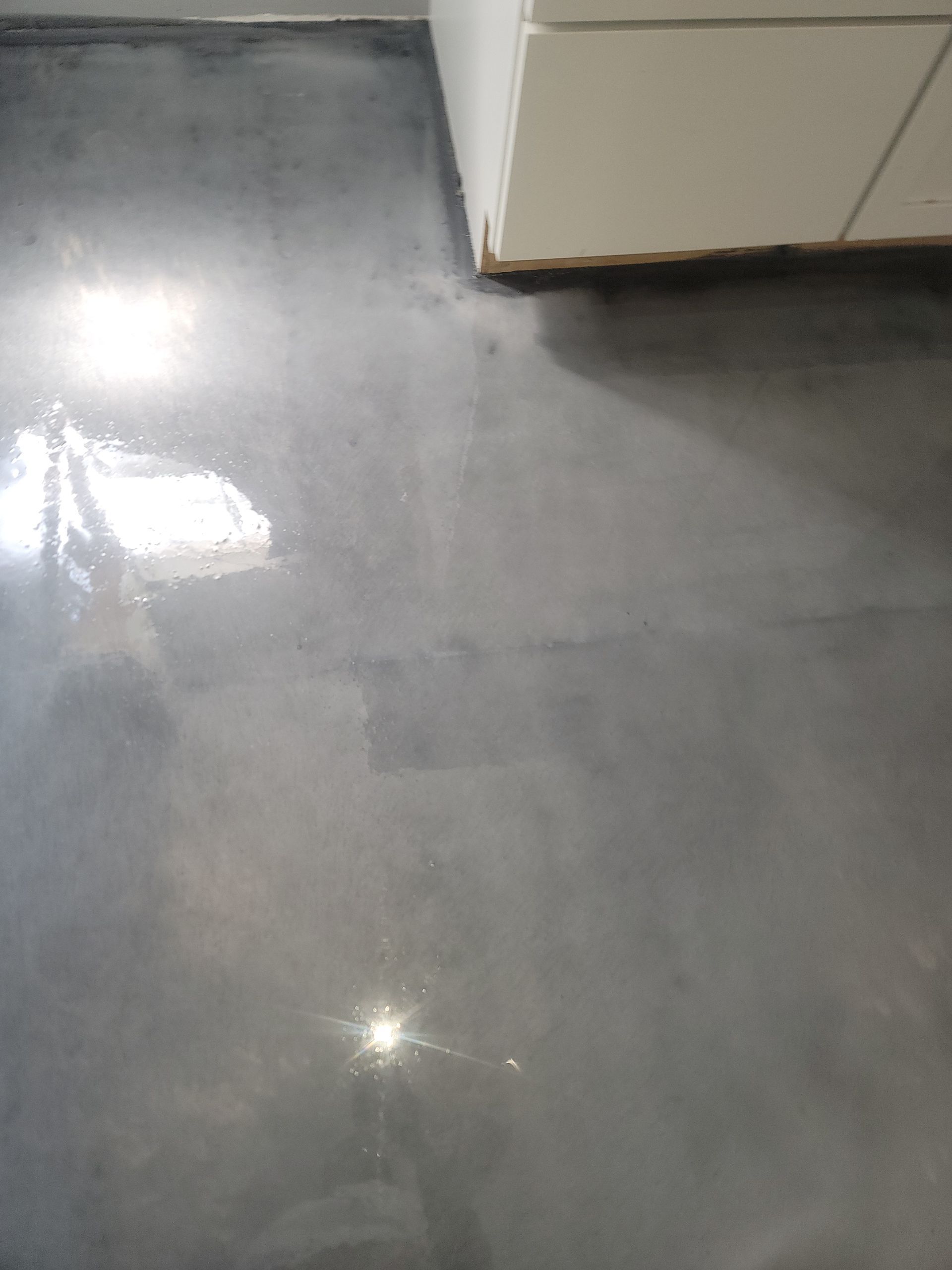 Glossy gray floor beside white cabinets, with bright light reflections.