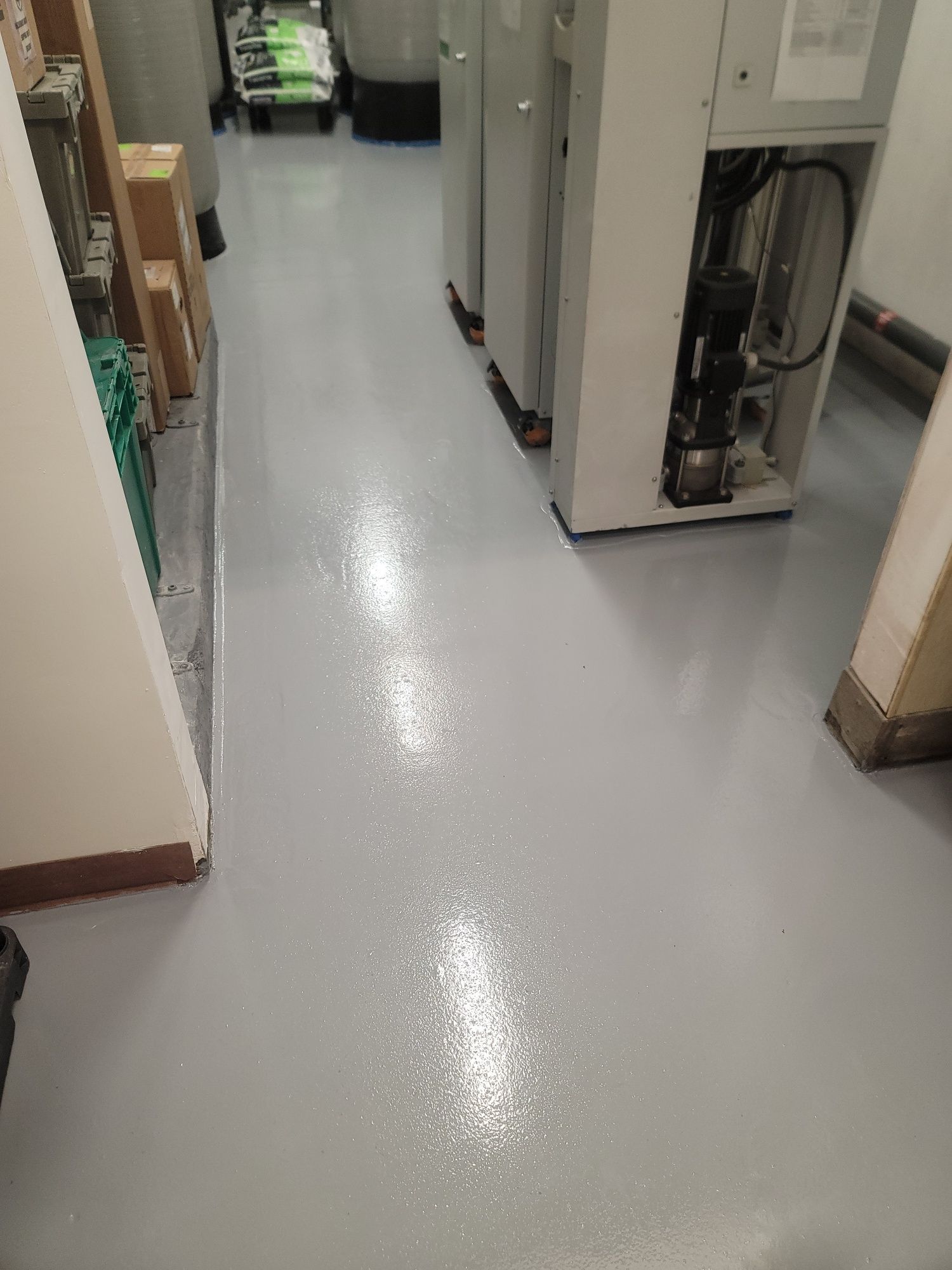 Narrow utility hallway with gray floor, open cabinets, and equipment storage along the walls.