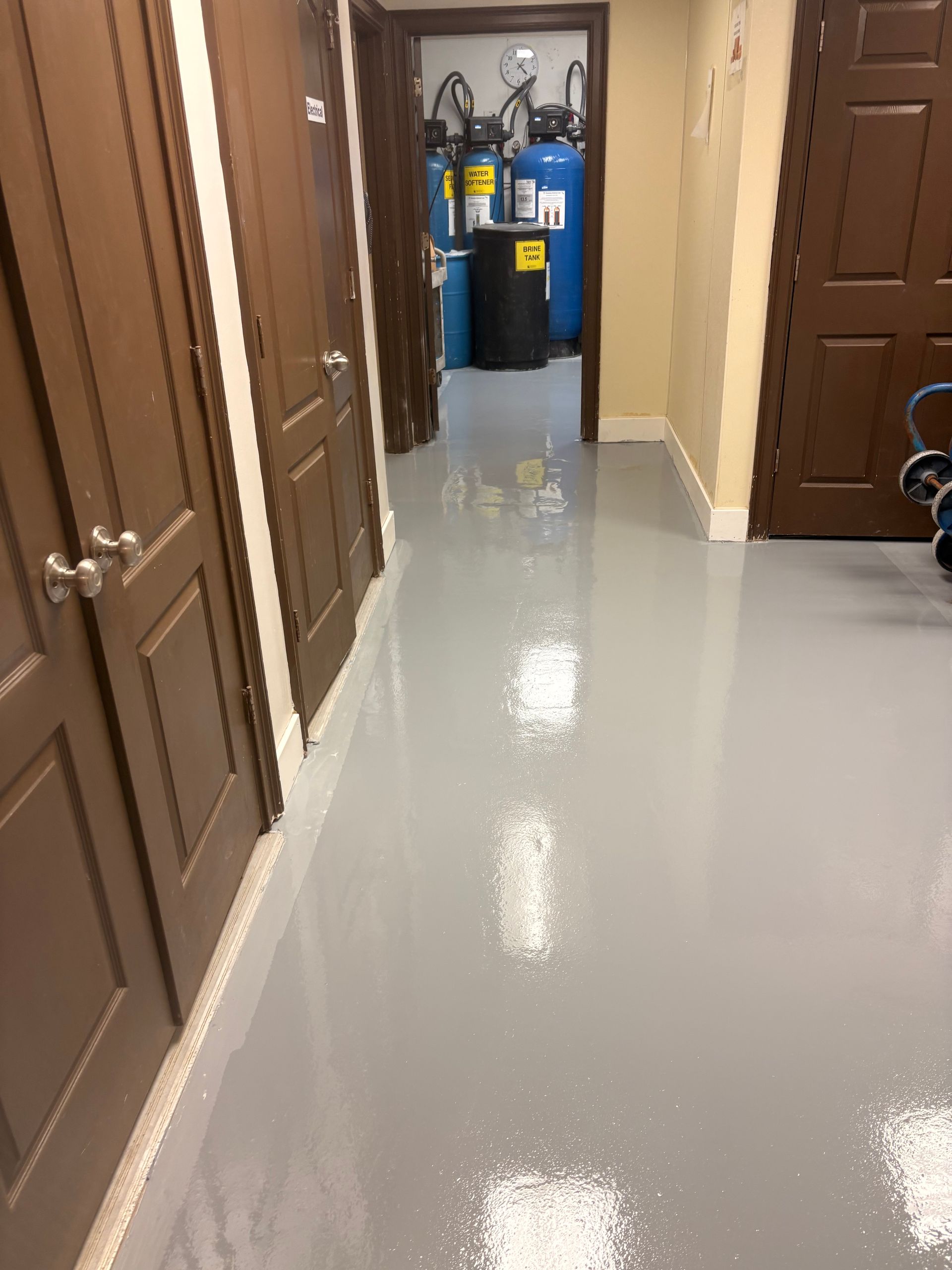 Hallway with brown doors and a gray floor, leading to a utility area with blue recycling bins.
