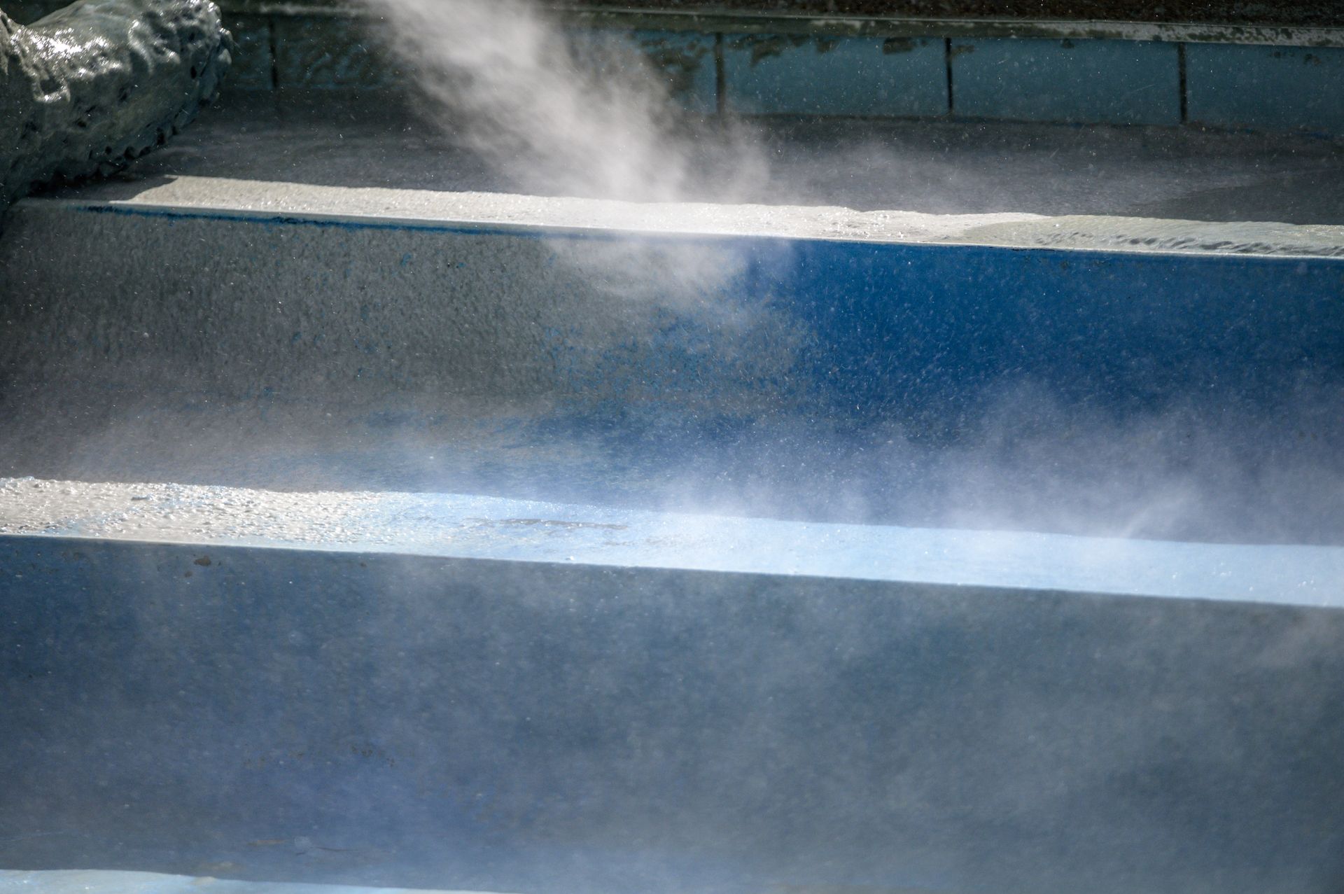 Steam rising from a blue road surface with white painted stripes.