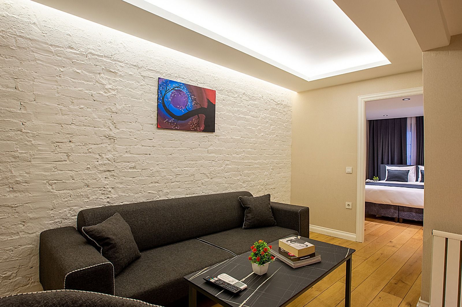 Gri kanepe, tuğla duvar, sanat eserleri ve yatak odasına bakan manzaraya sahip oda