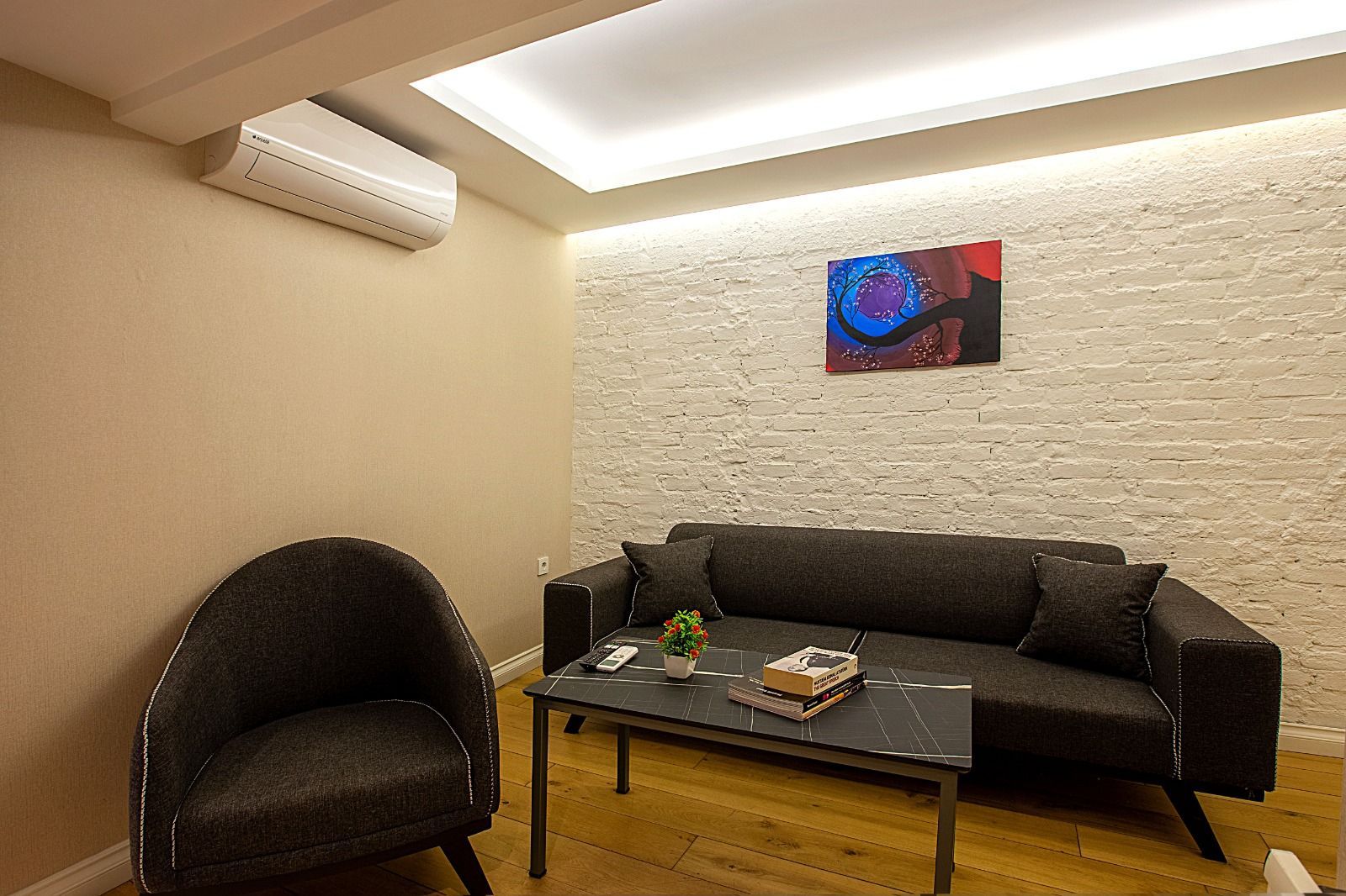 Modern living room with black sofa, chair, coffee table, wall art, and warm ceiling lighting