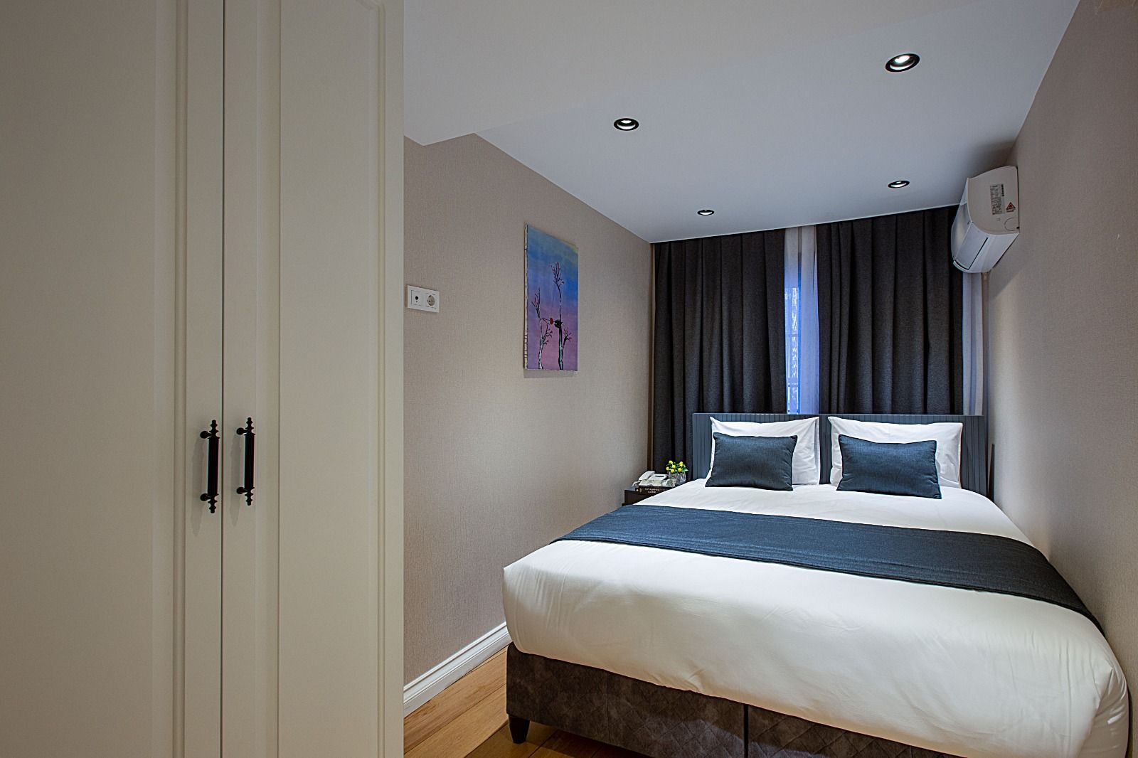 Modern bedroom with a white bed, dark curtains, wardrobe, and wall art