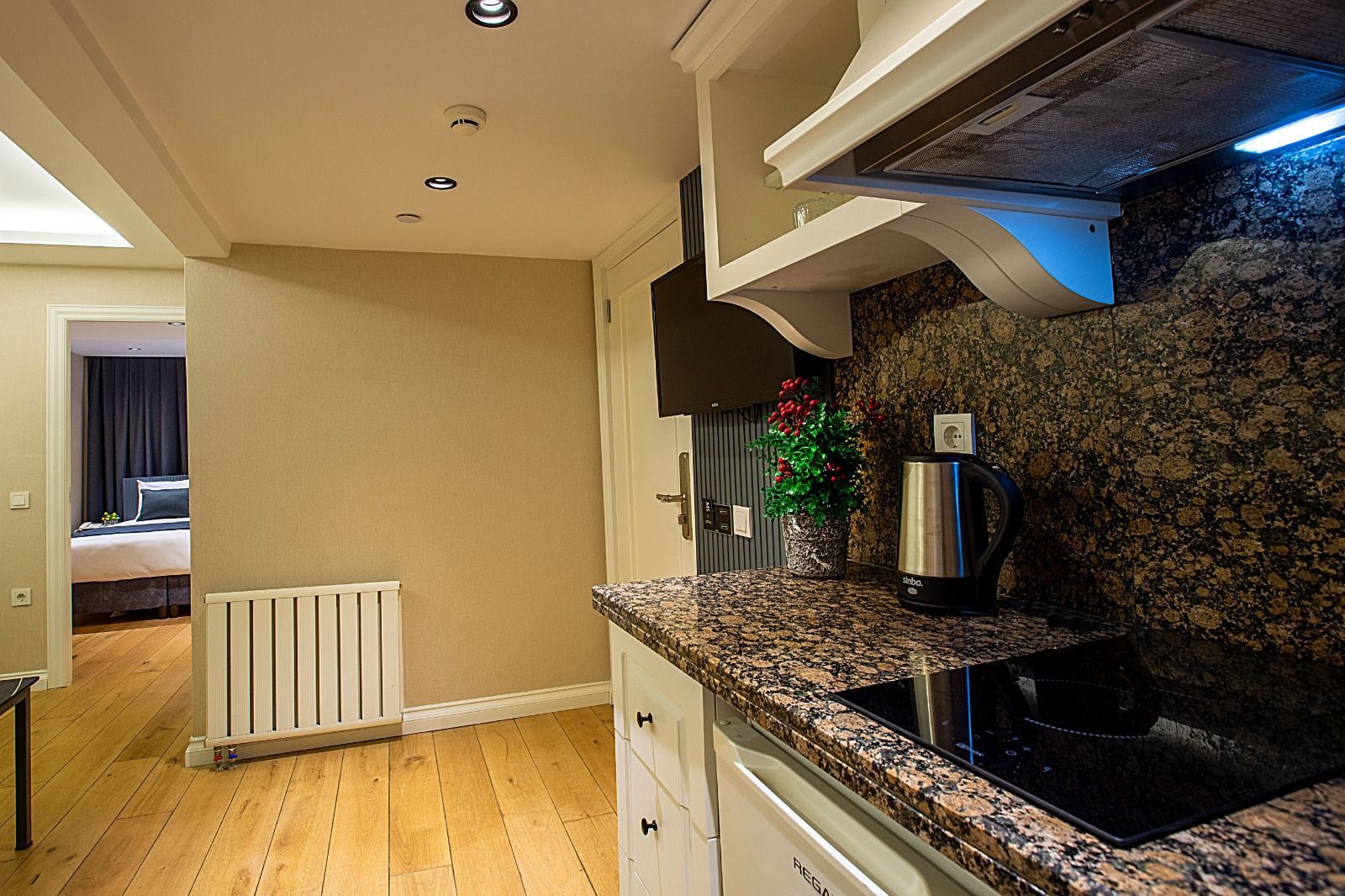 Modern kitchen with granite countertops, stainless sink, white cabinets, and wood flooring leading to a hallway