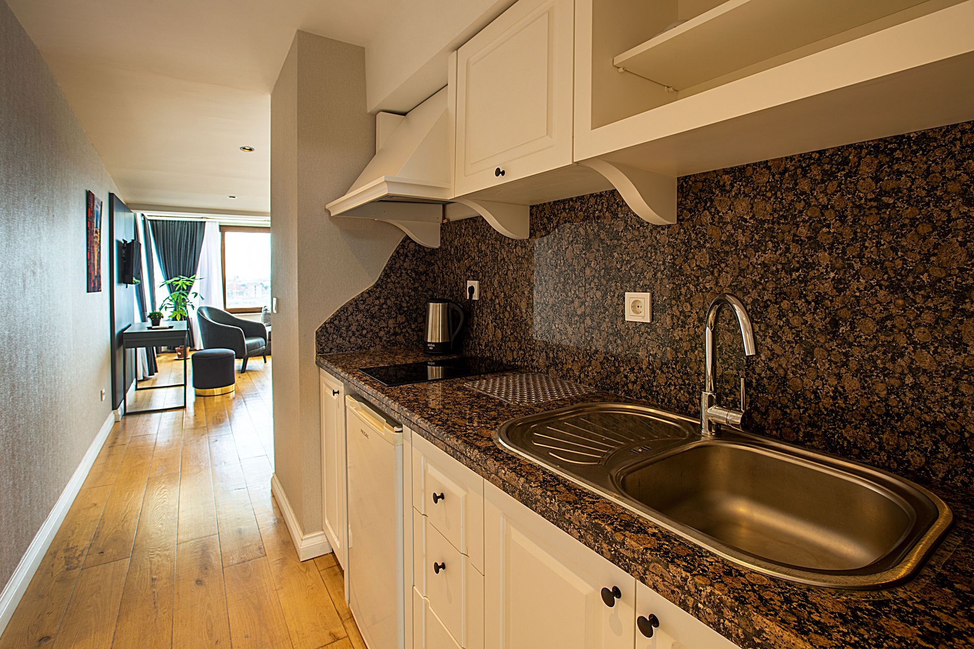 Narrow kitchen corridor with white cabinets, dark granite countertops, and stainless sink